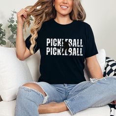 a woman sitting on a couch wearing a black shirt with the words pick'em all in white