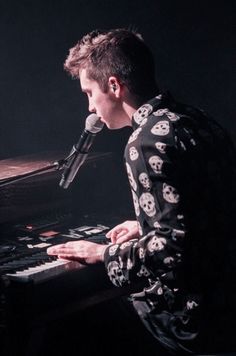 a man sitting at a keyboard with a microphone in front of him and skull print shirt on