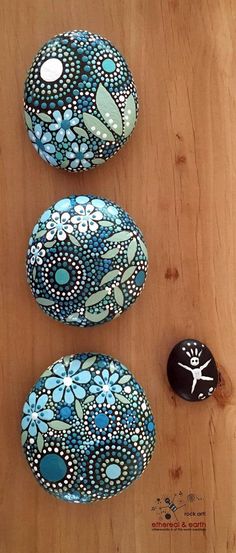 three painted rocks sitting next to each other on a wooden surface with white dots and blue flowers