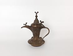 an antique bronze teapot with birds on the top and handle, sitting against a white background