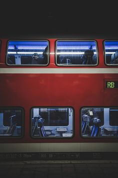 a red double decker bus parked next to a loading platform at night with its lights on