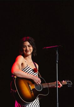 a woman holding a guitar in front of a microphone