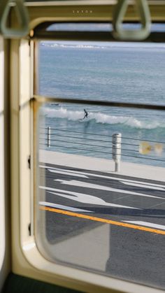 the view from inside a train looking out at the ocean and surfers in the water