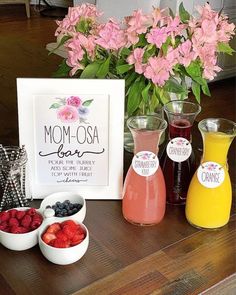 a table topped with fruit and drinks next to a vase filled with flowers on top of a wooden table