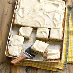 a pan filled with white frosted cake on top of a wooden table next to a knife