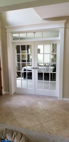 an empty living room with french doors leading to the kitchen and dining area in the background