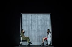 two people sitting on chairs facing each other in front of a wall with the door open