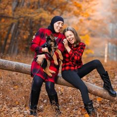 two women sitting on a log in the woods with their dog, both wearing plaid shirts and black boots