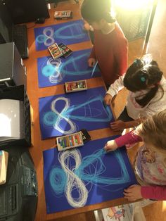 three children are drawing on blue paper with crayons