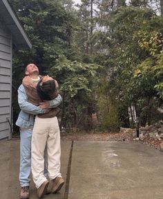 two men hugging each other in front of a house with lots of trees behind them