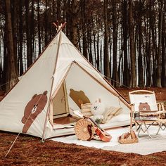 a tent set up in the middle of a forest with two chairs and a teddy bear pillow