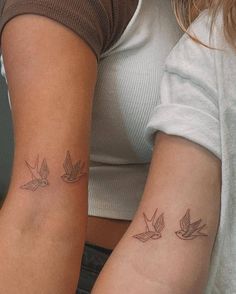 two women with matching tattoos on their arms, one has a bird and the other has a dove