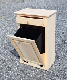 a wooden cabinet with a black trash can in the bottom drawer and one door open