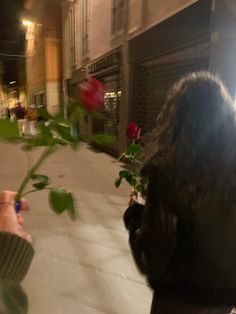 a person holding a rose in their hand and looking at it through the glass window