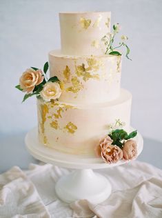 a three tiered wedding cake with gold leaf and flowers