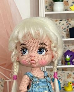 a close up of a doll with blonde hair and blue overalls in a room