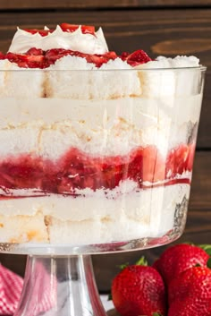 a layered cake with strawberries in it on a glass dish next to some strawberries