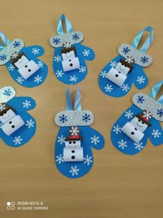 four paper snowmen are sitting on top of a table with blue and white decorations