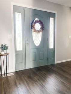 a door with a wreath on it in front of a wooden floor and side table