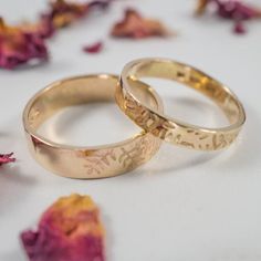 two gold wedding rings sitting next to each other on a white surface with dried rose petals