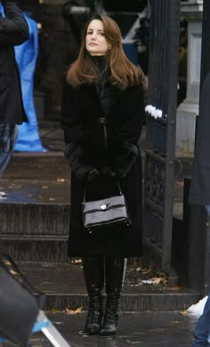 a woman in black coat and boots standing on steps