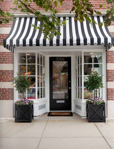 a black and white striped awning over a store front with potted plants outside