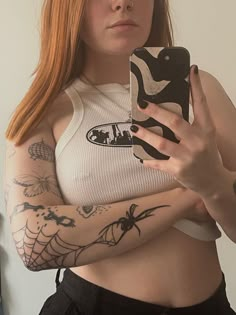 a woman with red hair and tattoos holding a cell phone up to her chest, looking at the camera