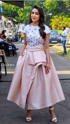 a woman in a pink dress standing on the street with her hands in her pockets