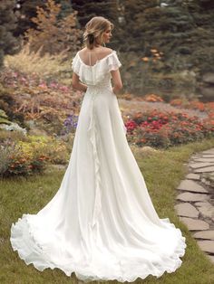 a woman in a white wedding dress standing on the grass with her back to the camera