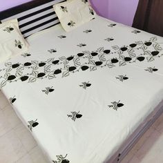 a bed with white sheets and black flowers on it in front of a purple wall