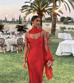 a woman in a red dress is standing on the grass near tables and palm trees