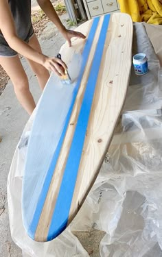 a woman sanding next to a surfboard on top of a plastic wrapper