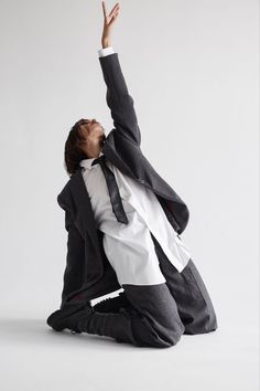 a man in a suit and tie sitting on the ground with his arms up to the sky