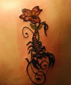 the back of a woman's shoulder with a scorpion and flower tattoo on it