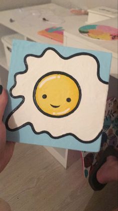 a person holding up a piece of paper with an egg in the shape of a smiley face