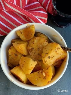 a white bowl filled with cooked potatoes next to a red and white striped napkin on top of a table