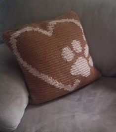 a crocheted dog paw pillow on a gray couch with a brown and white throw pillow