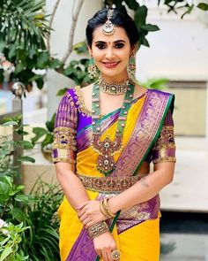 a woman in a yellow and purple sari with jewelry on her neck, smiling