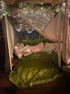 a canopy bed with green velvet sheets and pillows on it, surrounded by fairy lights