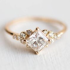 a gold ring with a princess cut diamond surrounded by small white and clear stones on the band