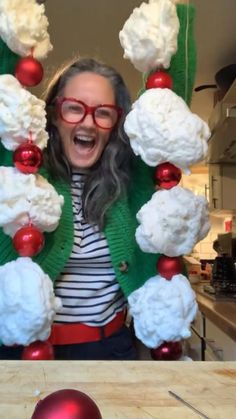 a woman wearing red glasses standing in front of a christmas tree with snowballs and balls