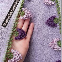 someone is holding their hand on the edge of a piece of fabric that has purple and green crocheted flowers