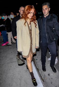 a man and woman are walking down the street at night, one is wearing a tan blazer