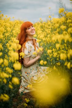 a woman with red hair is standing in a field of yellow flowers and smiling at the camera