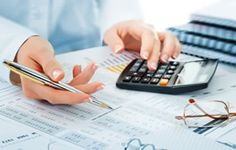 two people working at a desk with calculator, glasses and pen on it