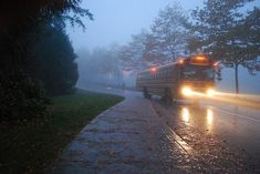 a school bus driving down a rain soaked road in the evening with its headlights on