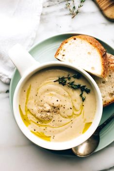 a bowl of soup on a plate with bread and herbs next to it, ready to be eaten