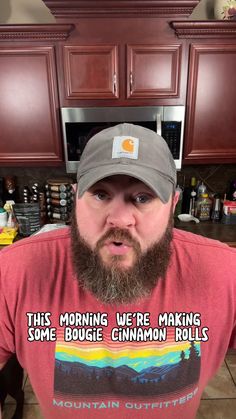 a man with a beard wearing a red shirt and gray hat in front of brown cabinets