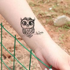 a small owl tattoo on the left arm and wrist is shown in front of a wire fence