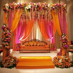 an orange and pink wedding setup with flowers on the stage, couches and pillows